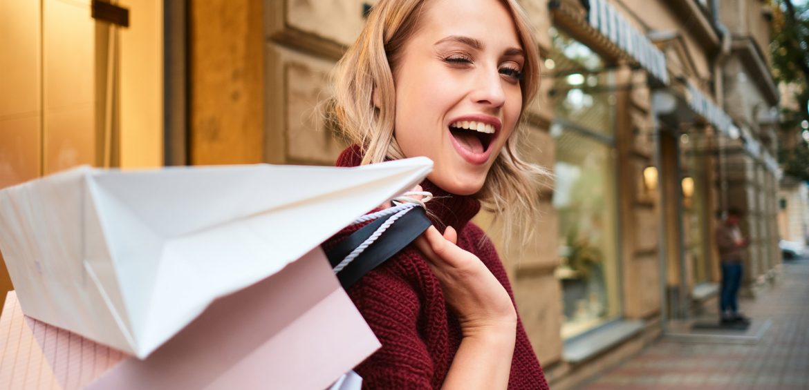 Portrait of cheerful blond girl with shopping bags happily winking out on city street